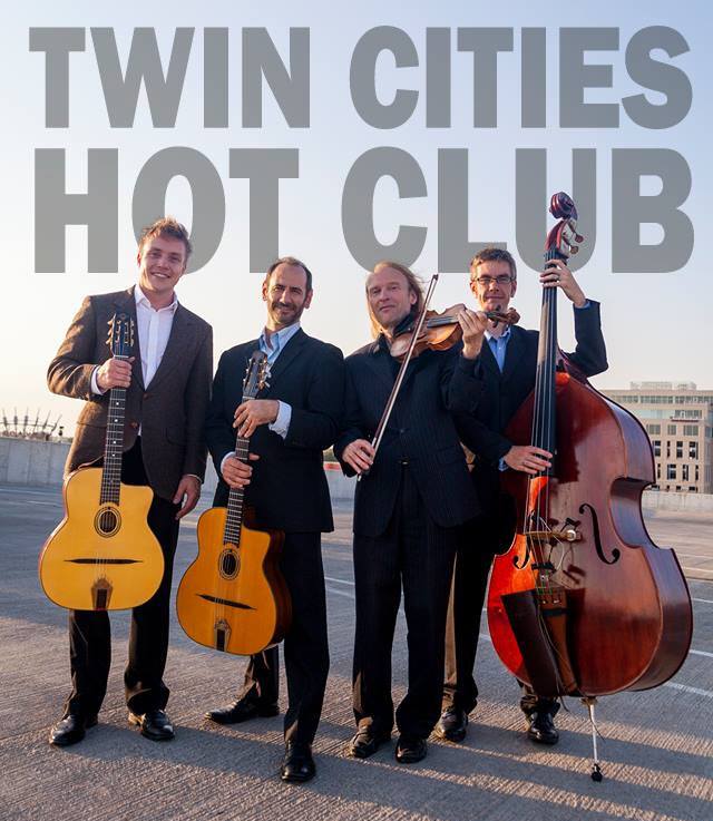 Photograph of the Twin Cities Hot Club standing on an urban rooftop.  Stan Ponkin, guitar.  Robert Bell, guitar + bandleader.  Gary Schulte, violin.  Matt Peterson, bass.