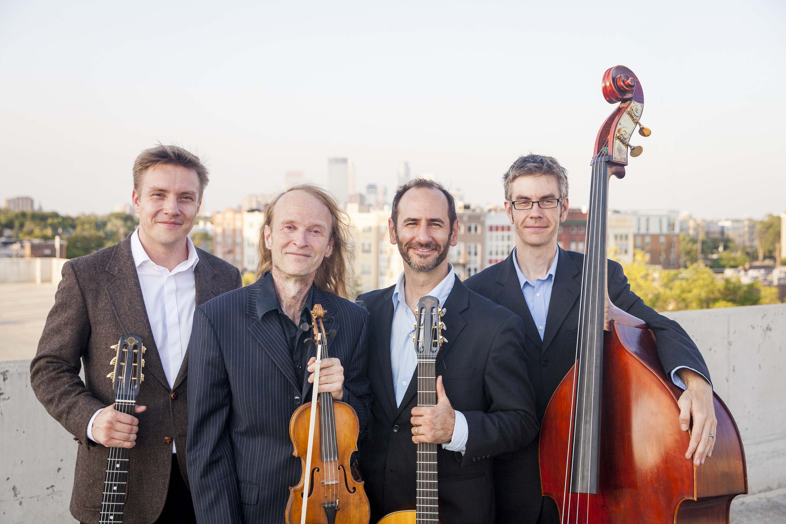 Photograph of the Twin Cities Hot Club standing on an urban rooftop.  Stan Ponkin, guitar.  Gary Schulte, violin.  Robert Bell, guitar + bandleader.  Matt Peterson, bass.