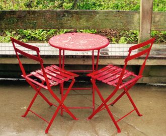 Two red metal chairs and a small red metal table, full of shining raindrops.