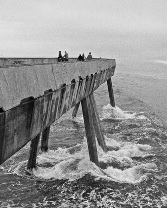 A long pier in tossing seas, people looking over the railing, in black and white.