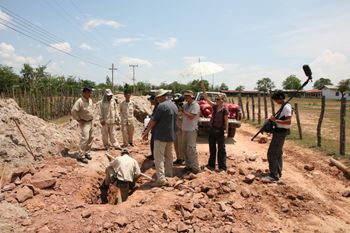 Director/cinematographer Kim Mordaunt, producer Sylvia Wilczynski & sound recordist Dan Miau film bomb disposal team who have discovered a bomb in the road between 2 schools, Savannakhet, Laos
