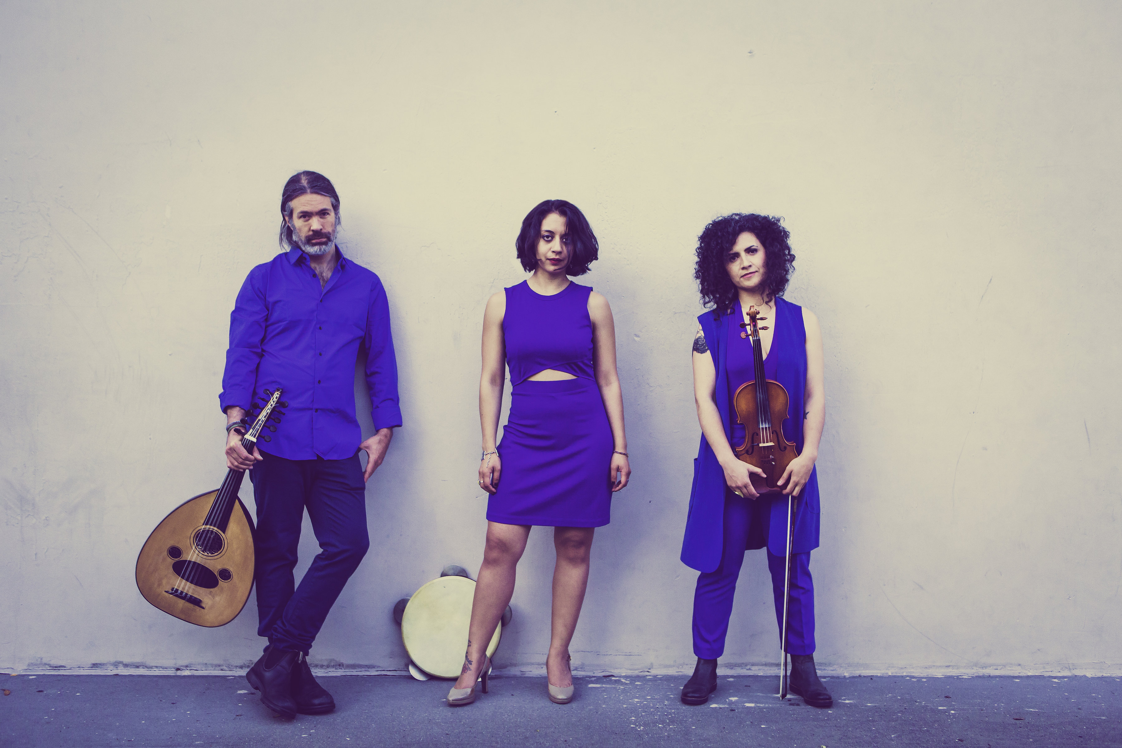Adam Good holding oud, Jenny Luna with frame drum, Eylem Basaldi with violin — dressing in blue against white background
