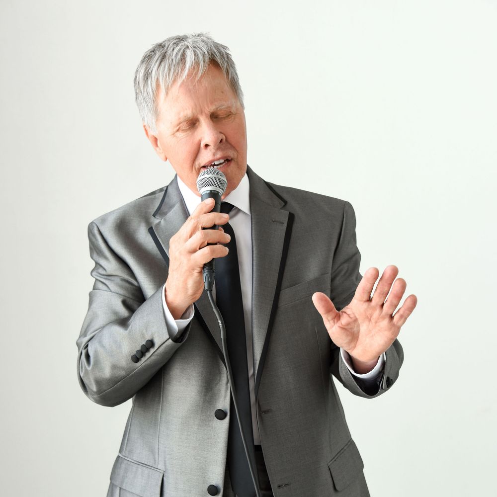Jim Gerber singing a gospel tune wearing a silver suit and holding a microphone