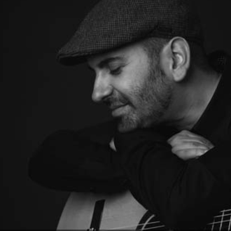 Foto ritratto in bianco e nero di Giacomo Deiana appoggiato alla chitarra classica. 