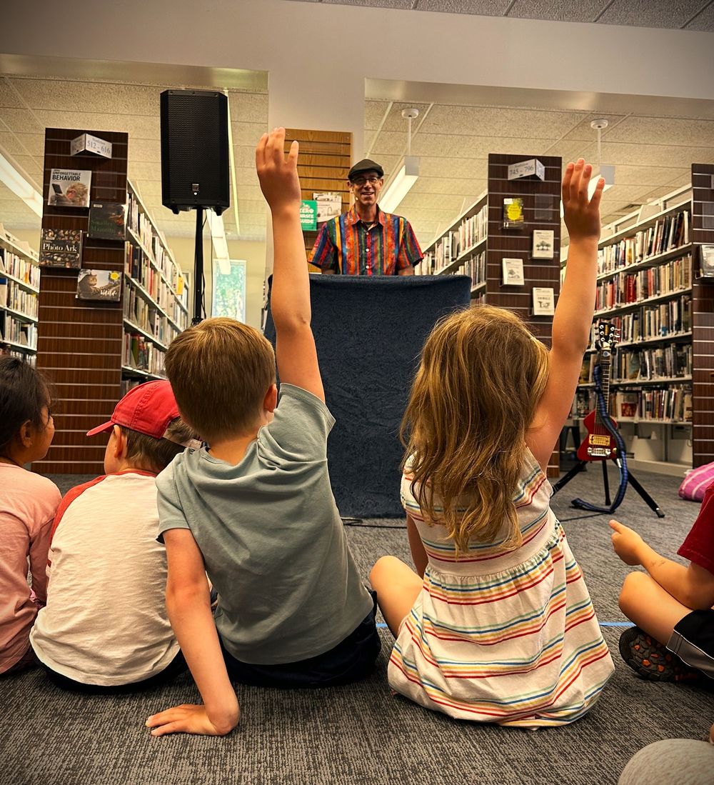 Children raising their hands during an interactive Library Boogie performance inside a public library