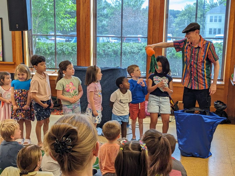 Children actively participating in Tom Knight’s Library Boogie program at a public library, singing and engaging with puppets