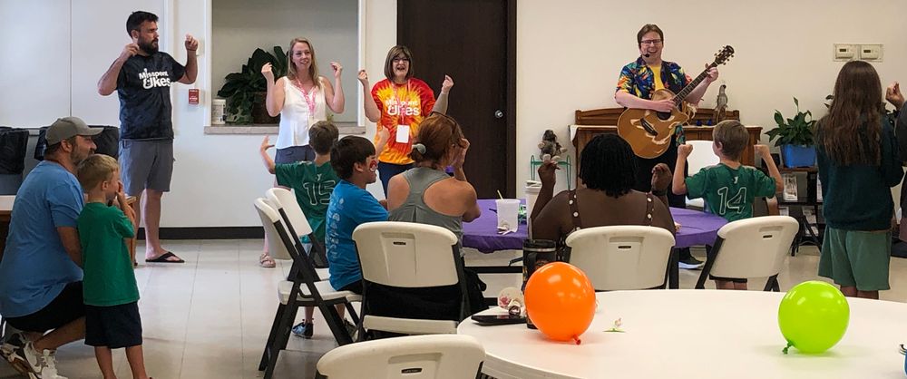Monty performs in the KidZone at the Dancing Turtle Arts Festival in Stillwater, OK, June 2026. This photo shows kids and adults performing sign language while Monty sings "The Cat Came Back"