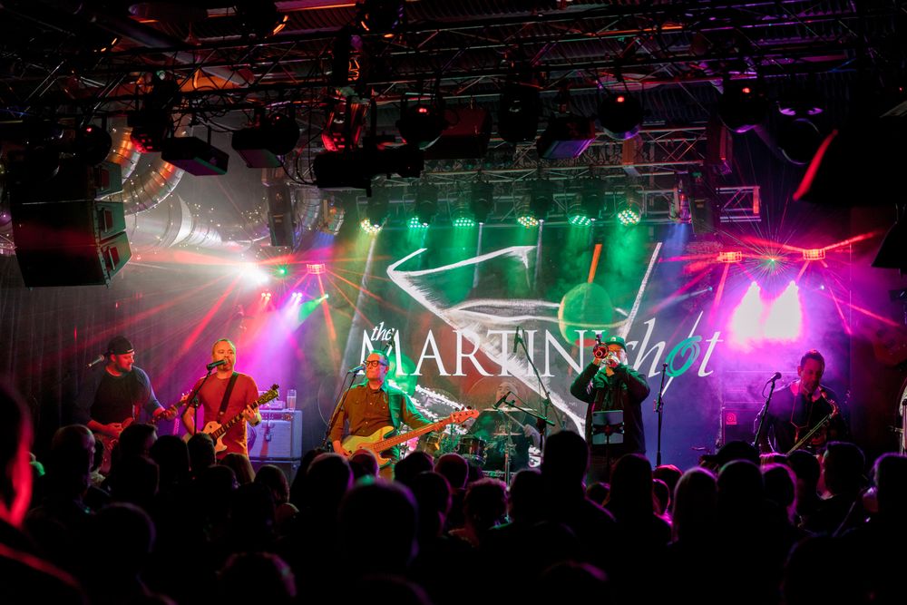 The Martini Shot horn-driven party band performing live on stage with full lighting and high-energy atmosphere