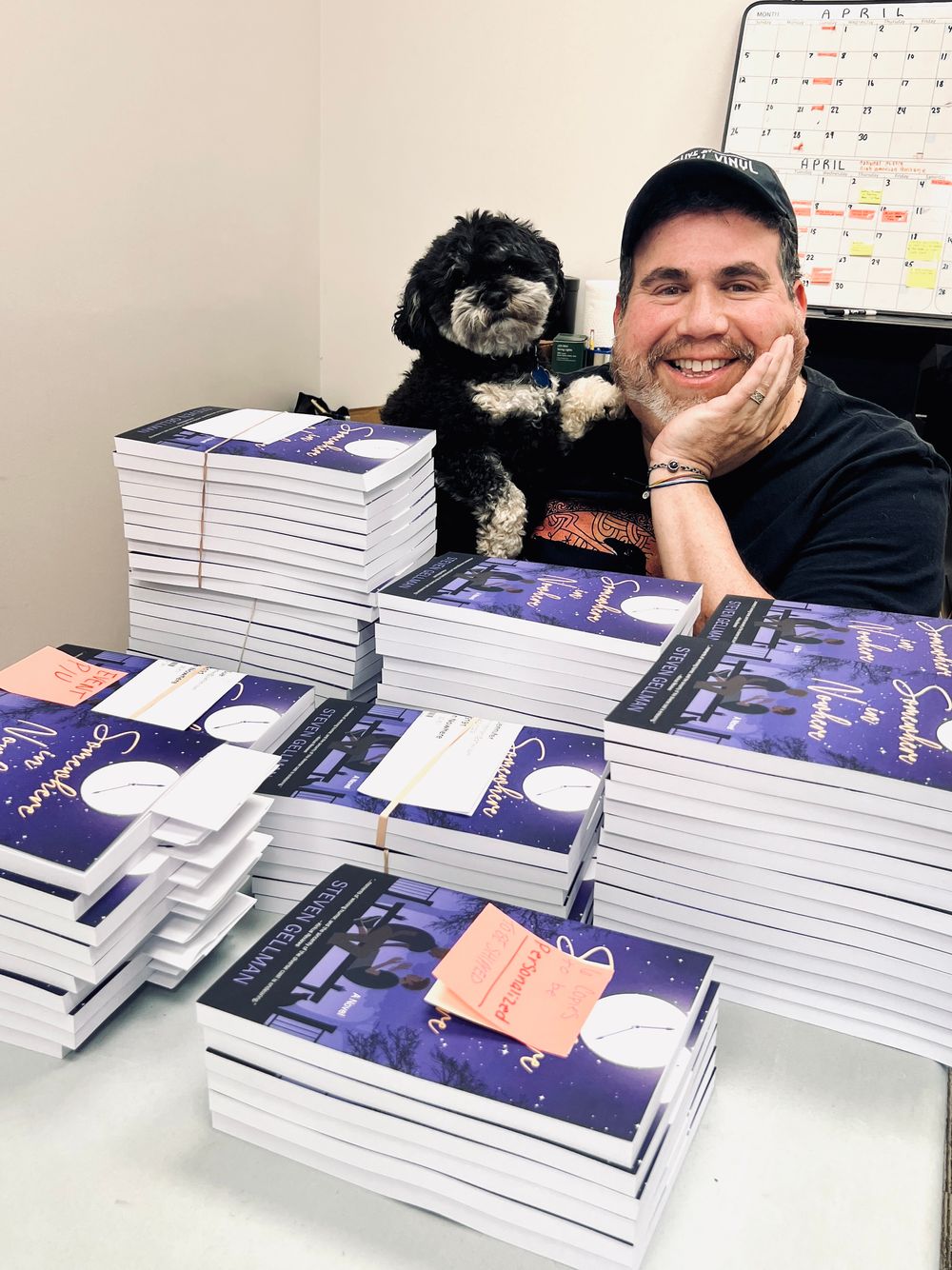 Steven Gellman sits a table with his rescue dog, Oscar, signing stacks of books prior to his book launch event. 