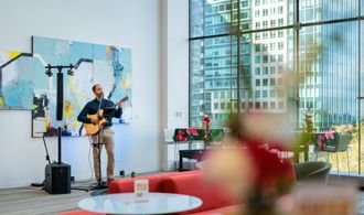 Solo musician performing live acoustic guitar and vocals in a modern indoor venue with large glass windows and abstract artwork.