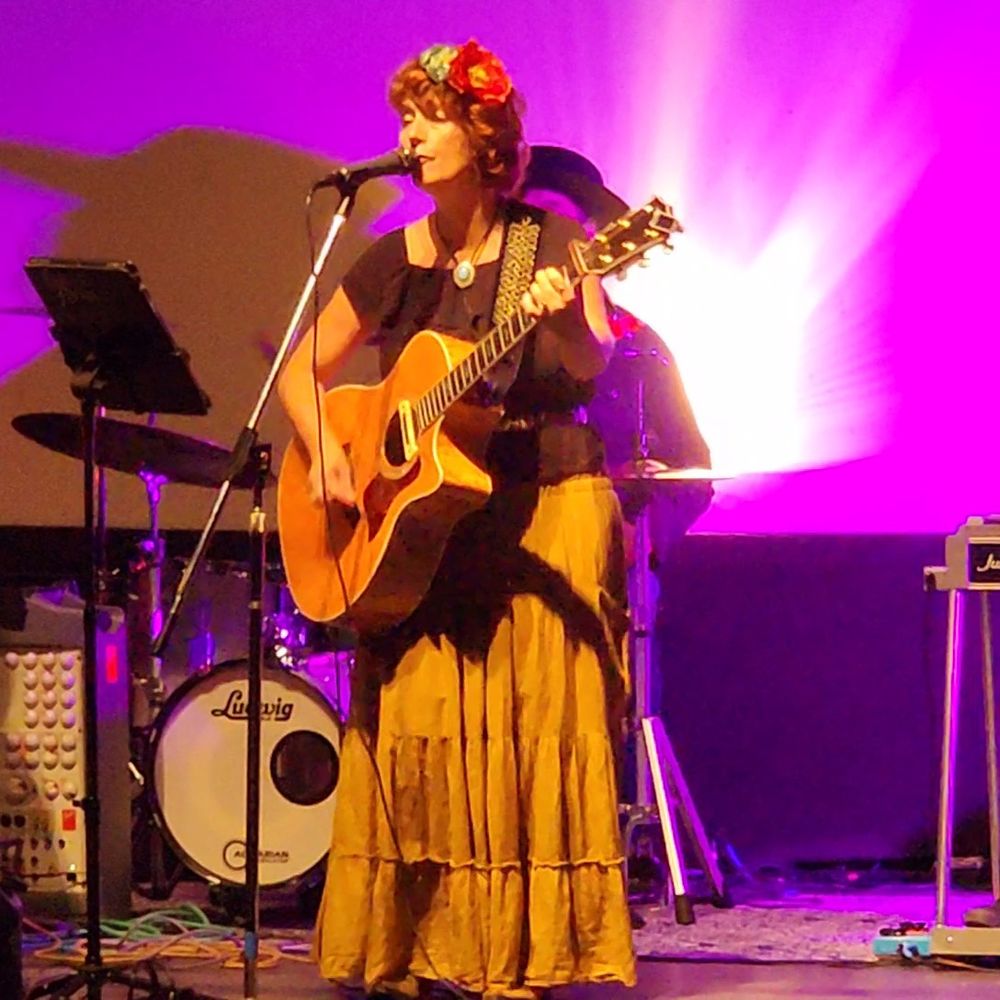 Heather Richards performing live on stage with acoustic guitar and floral crown during a concert appearance
