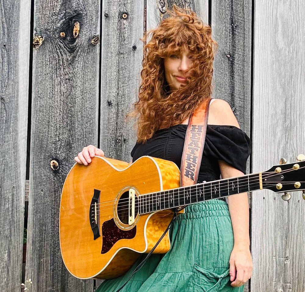Heather Richards holding guitar beside weathered wood