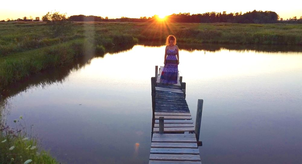 Heather Richards standing on a wooden dock at sunset beside calm water and open countryside