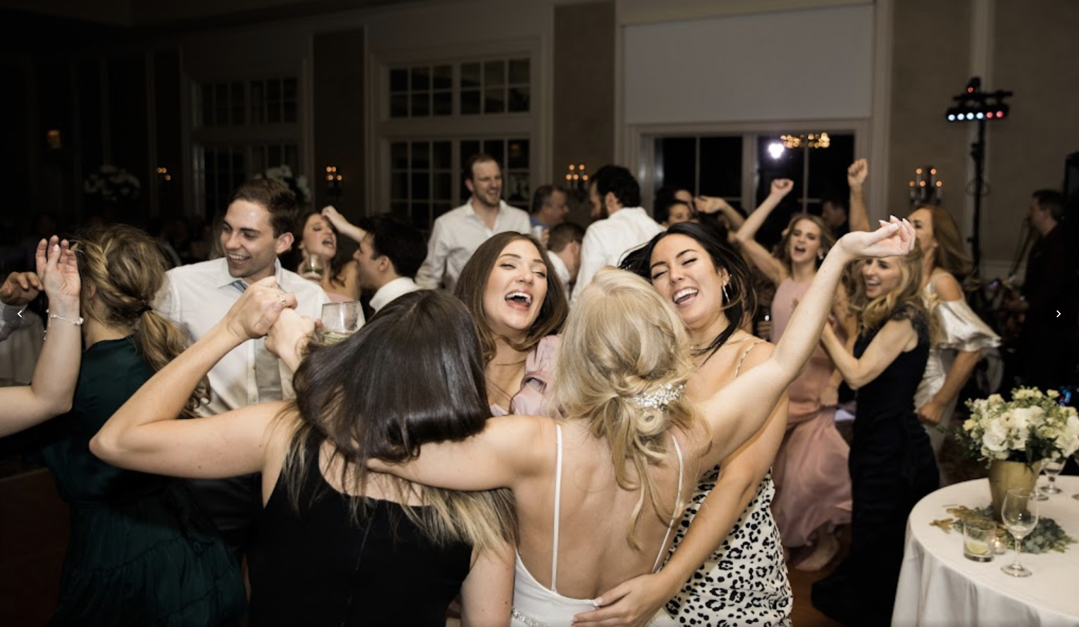 Bride and friends laughing on a packed wedding dance floor