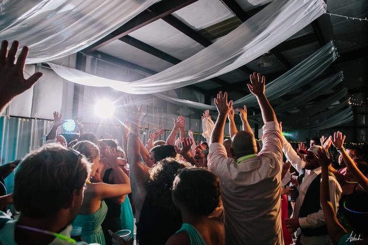 Packed wedding dance floor, guests with hands in the air while 7 Sharp 9 plays, bridesmaids in teal