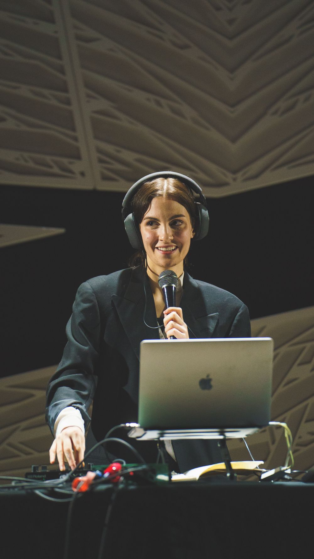 Medusa wears headphones and smiles over a microphone, surrounded by music equipment, on the stage of National Sawdust