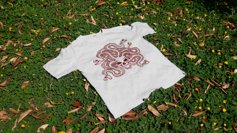 A white T-shirt with a skeleton "Medusa" logo lies on the grass at night.