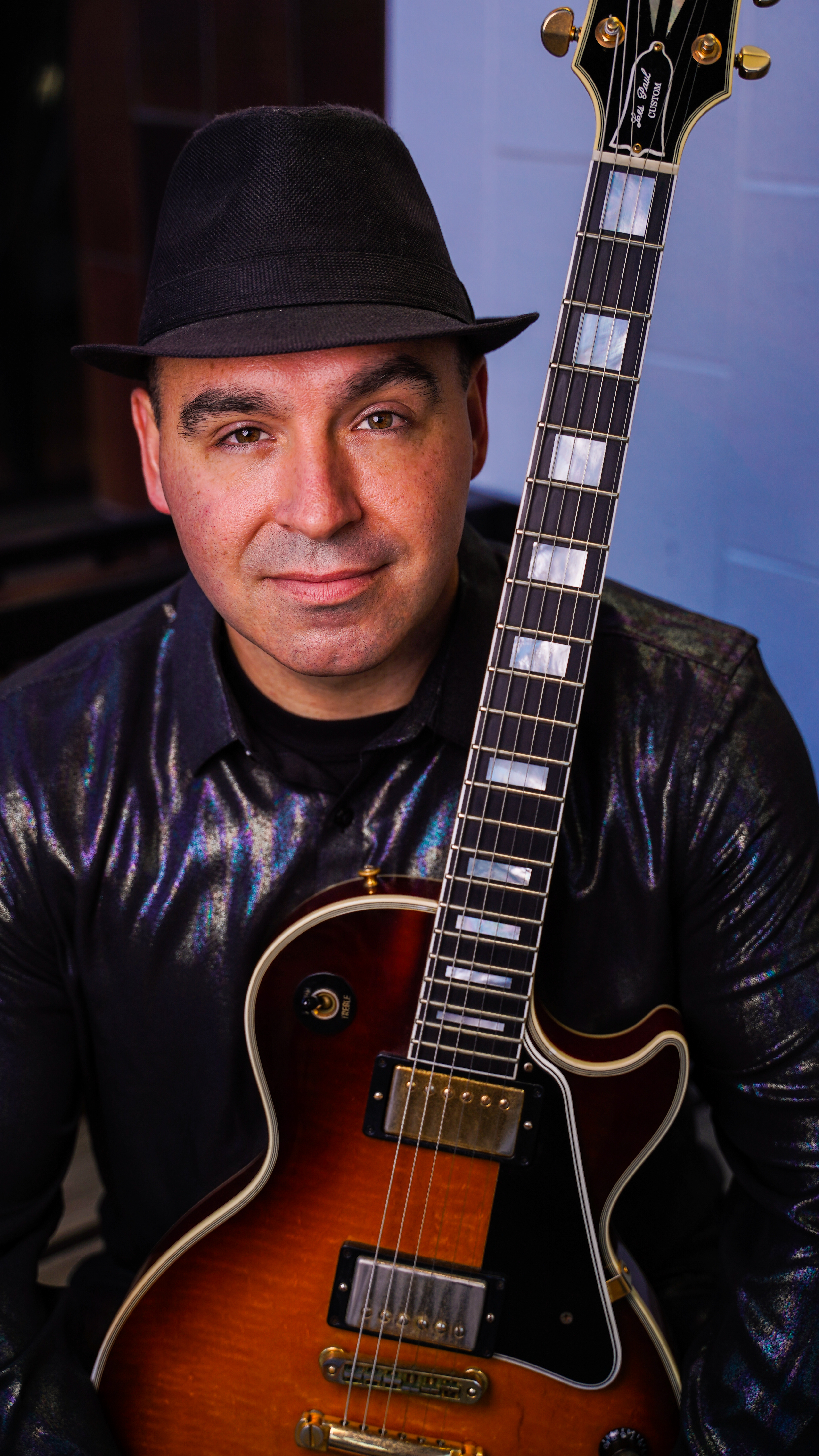 Paul Steward in a black fedora holding his Les Paul guitar
