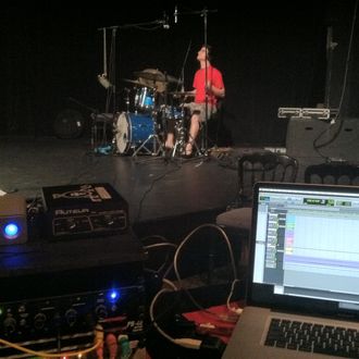 A red shirted drummer plays a blue sparkle Rogers drumset with a ProTools rig in the foreground