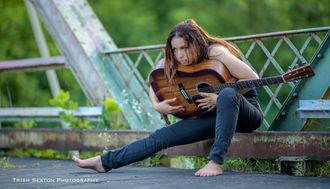 Beth Arnold Gilbert with acoustic guitar sitting on bridge in bare feet