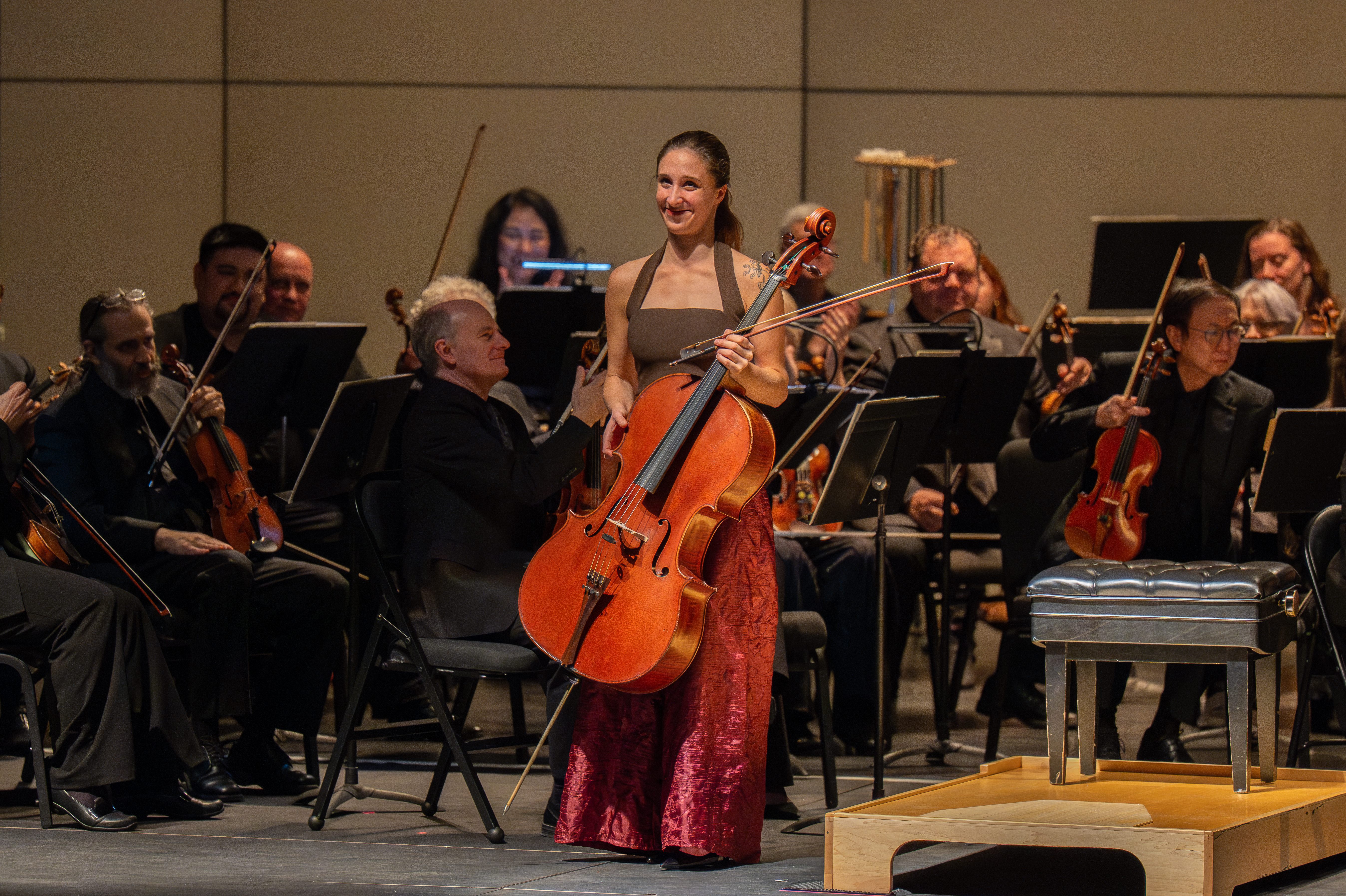 Cellist Annie Jacobs-Perkins, a smiling white woman standing in front of orchestra holding her cello
