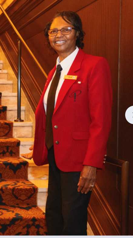 Smiling Black woman with glasses in a red usher's jacket standing inside the concert hall