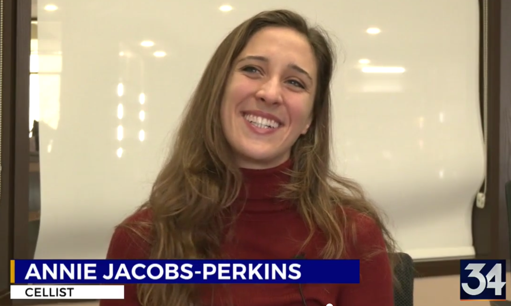 Annie Jacobs-Perkins, a smiling white woman with long brown hair in a red turtleneck sweater