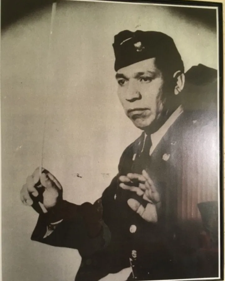 Boyd Eagle Piatote, a Native American man in military uniform, holding a baton with both hands raised