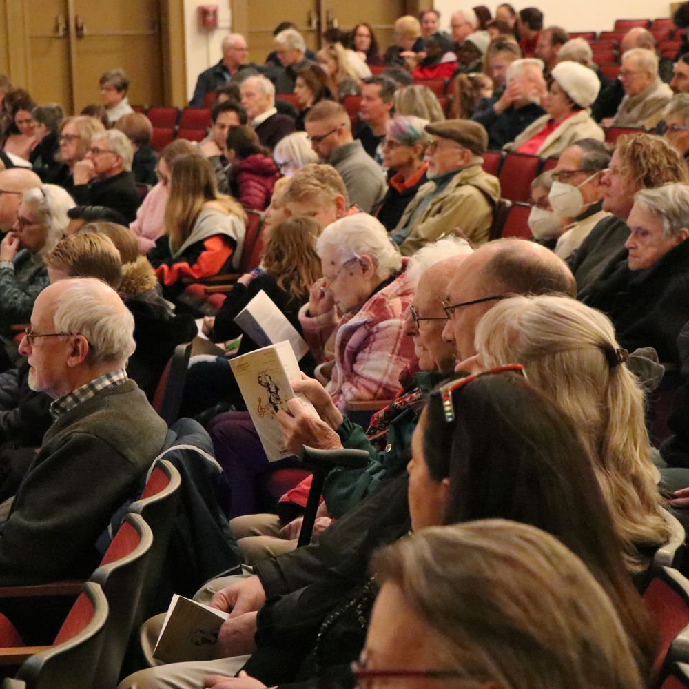 Audience members of various ages sitting in their seats at the Broome County Forum Theatre, some reading programs
