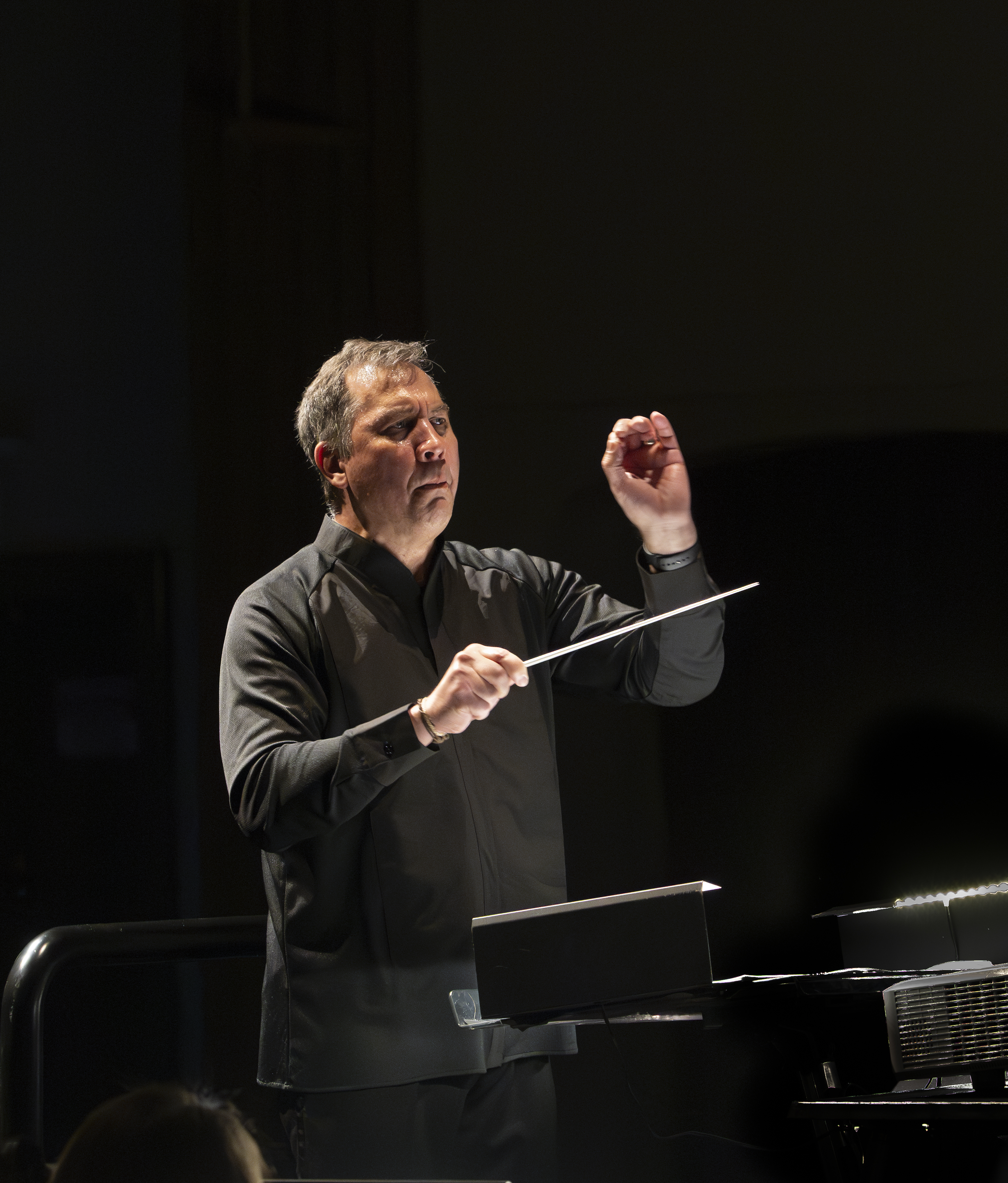 Maestro Daniel Hege, a Native American man wearing all black, conducting with a baton