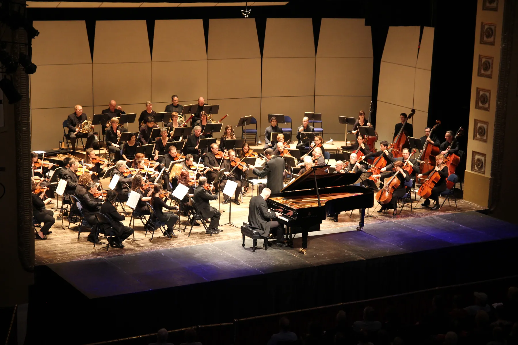An orchestra onstage with a white-haired male soloist playing a grand piano in front