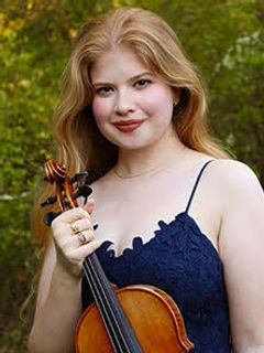 Image: Violinist Sophia Werner, a white woman with long red hair in a navy blue camisole top holding a violin