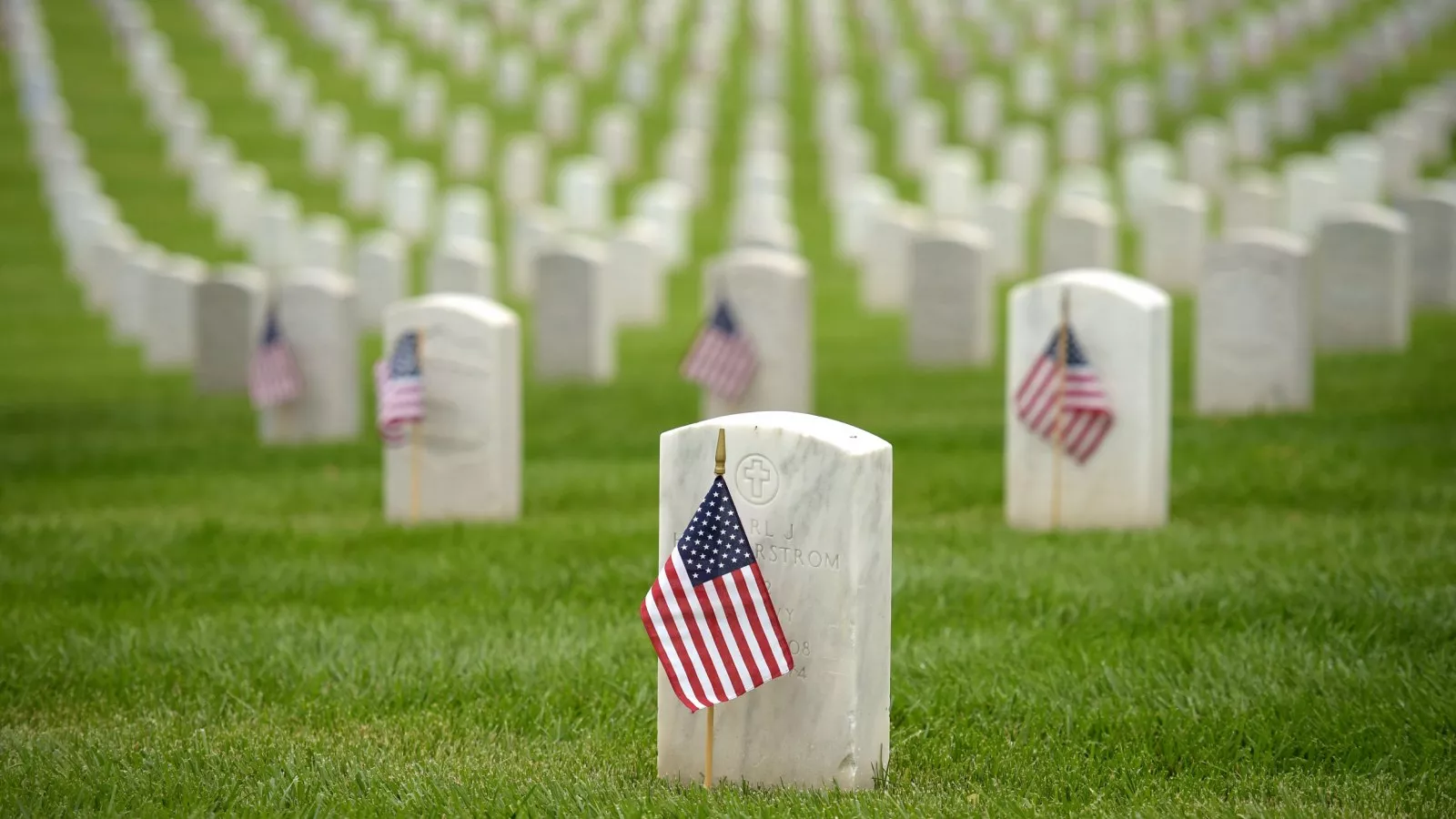 Image: A military cemetery with many uniform white gravestones decorated with American flags