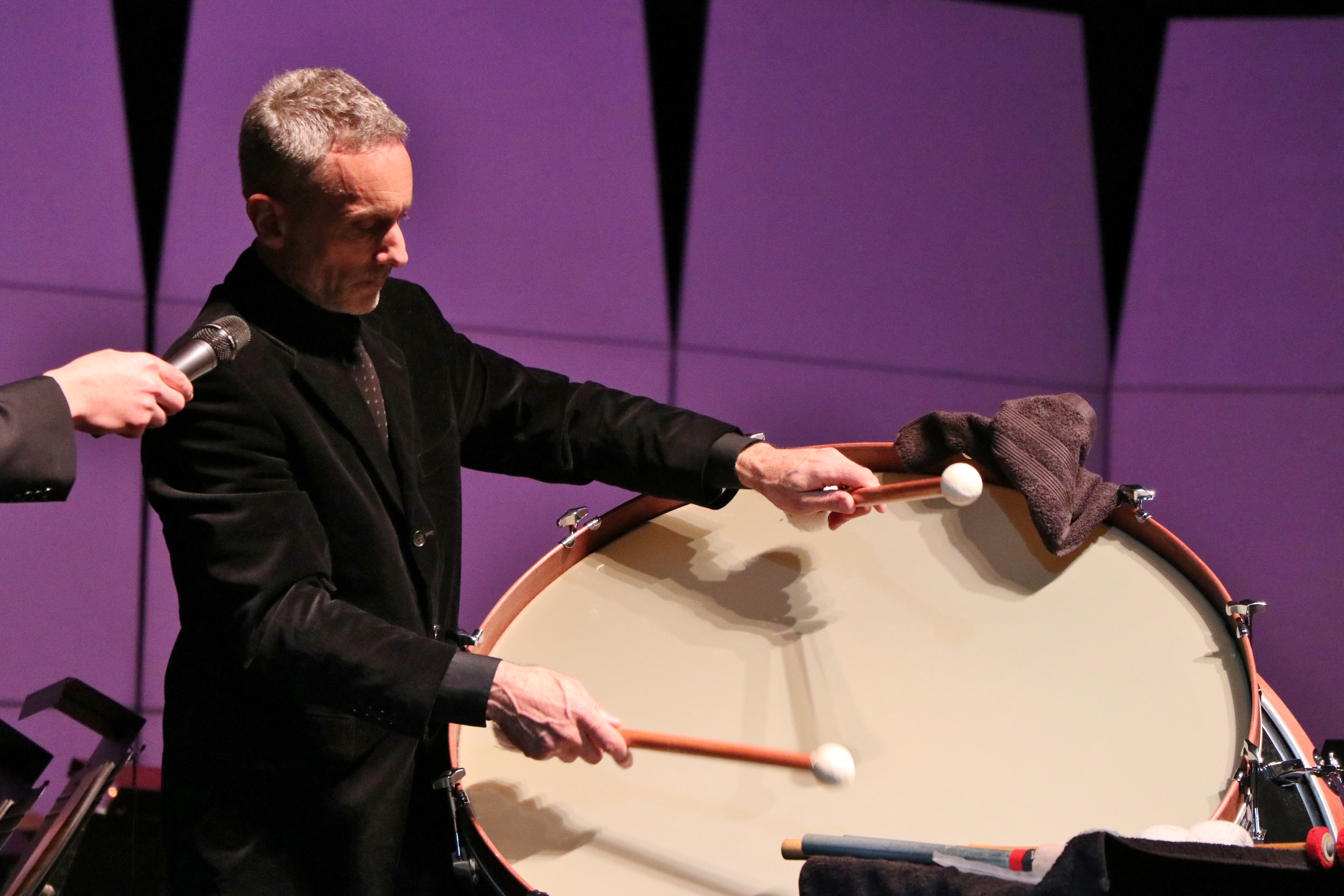 Principal Percussionist Sam Lazzara, a white man with gray hair wearing black, playing a bass drum with mallets