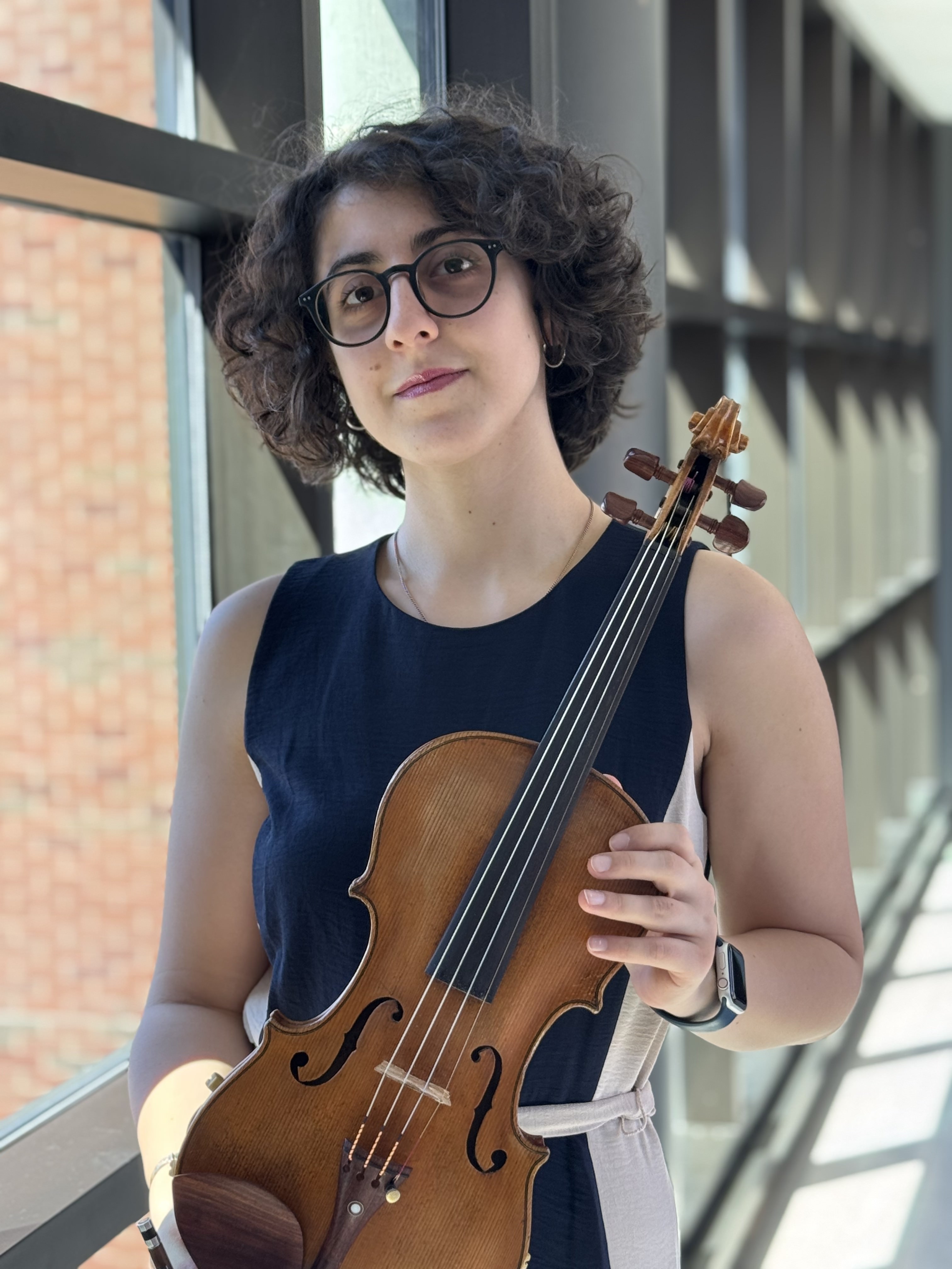 Salome Lomidze, a white woman with glasses and short curly dark hair in a blue sleeveless dress and glasses, holding a violin