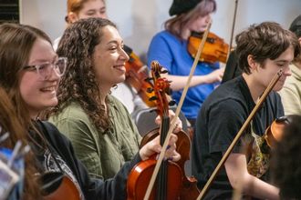 image: violinist Emily Garrison sitting among high school string players