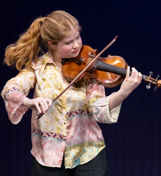 image: violinist Sophia Werner, a young, red haired women holding a violin in an outdoor setting