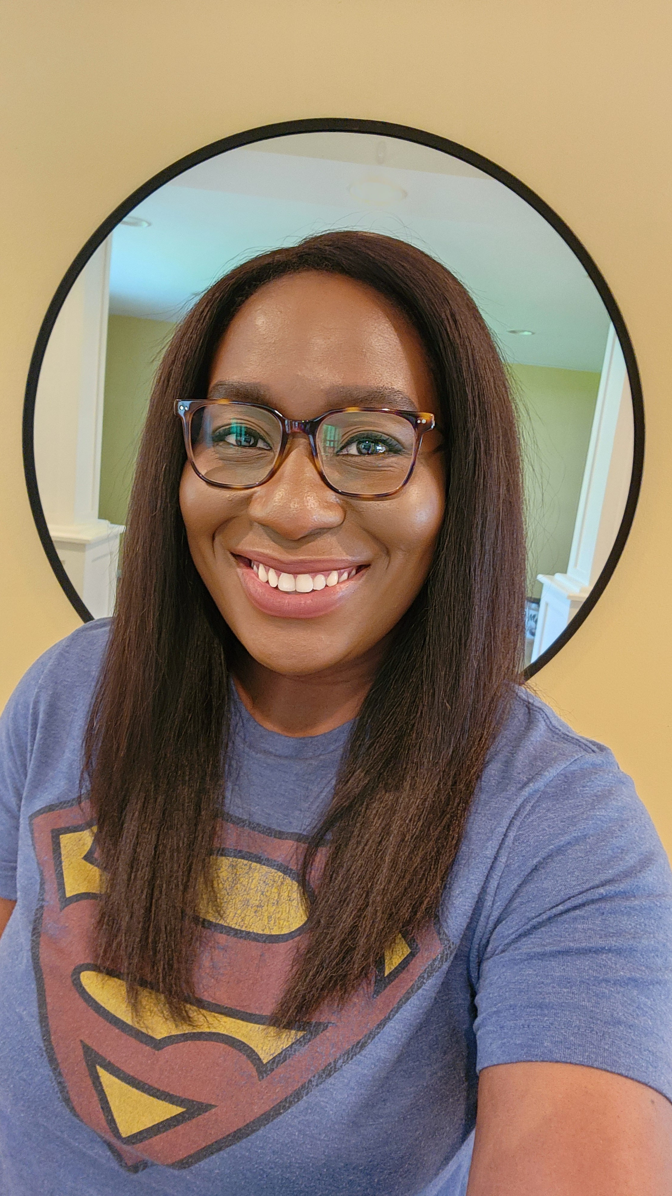 Dr. Funmi Atilola, a smiling Black woman with long brown hair and glasses wearing a Superman t-shirt