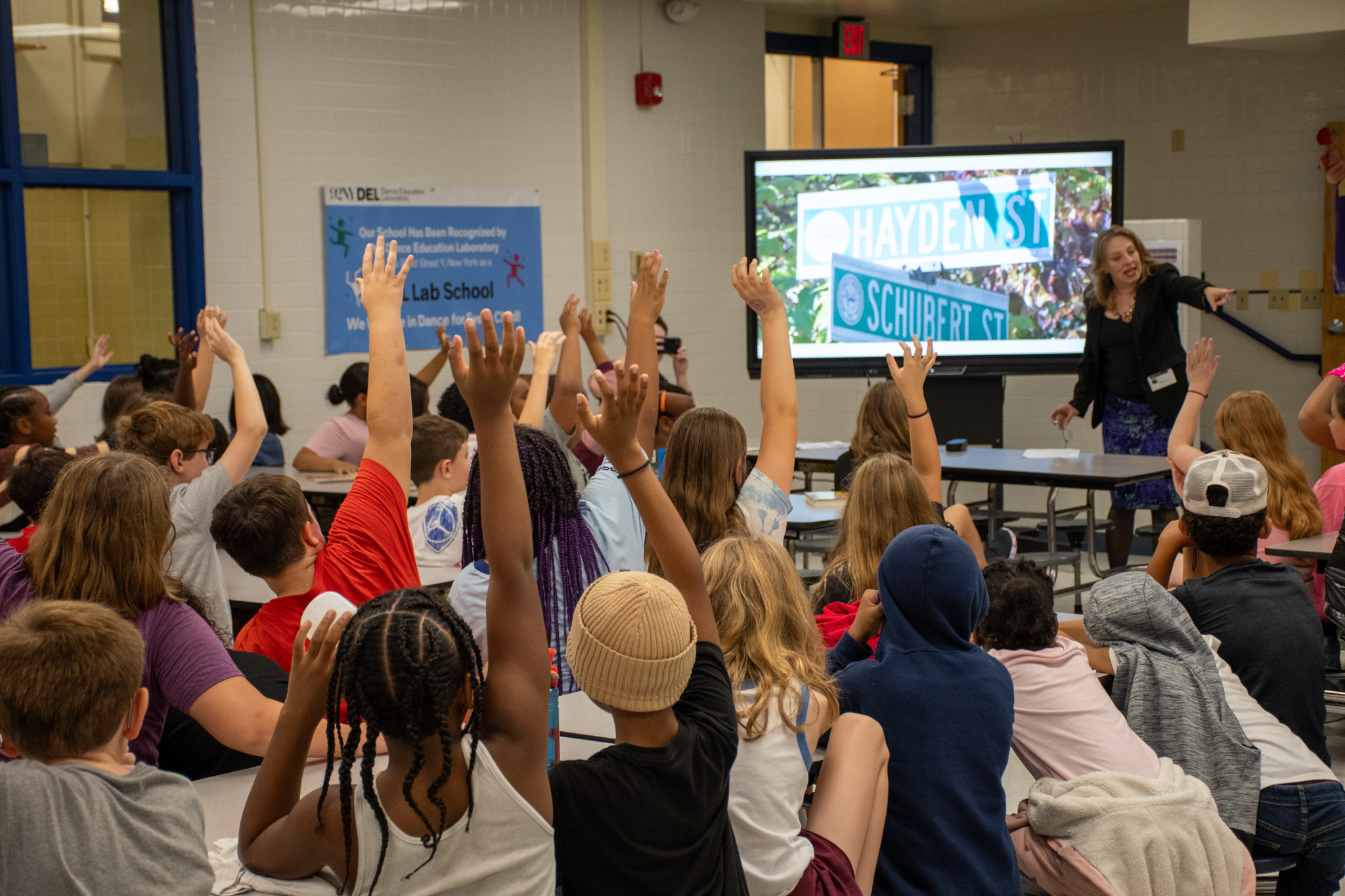 Julia Grella O'Connell, a white woman with brown hair, calling on an elementary school student in a classroom of children with hands raised