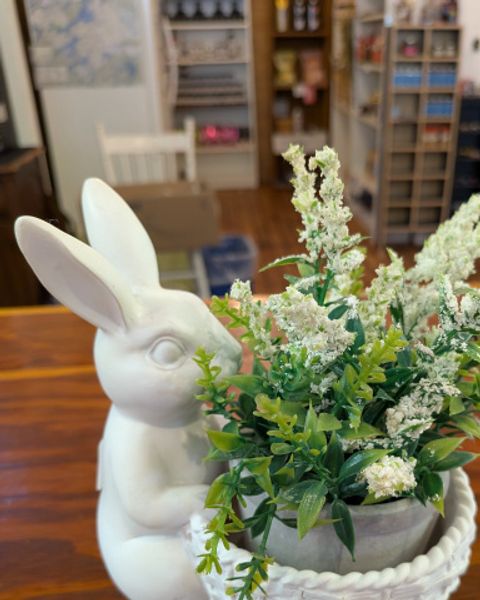 A white pottery rabbit sitting and holding a basket with white and green flowers