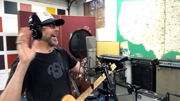 Scott Hall musician and songwriter in the studio holding a three string solid body guitar
