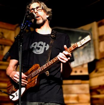 Scott Hall musician and songwriter singing and playing a three string solid body guitar live

