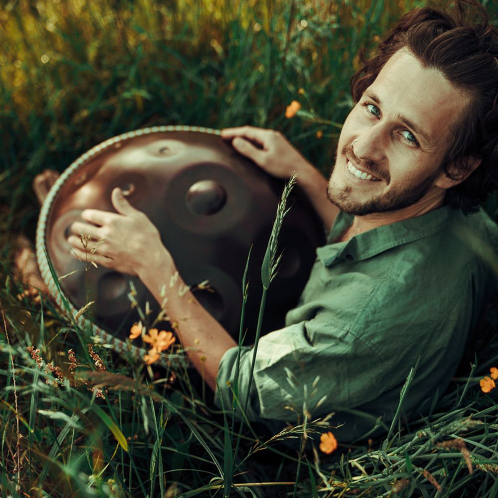 Alexander Mercks liegt lächelnd mit seiner Handpan im Gras – Schnupperworkshop Handpan bei Freiburg