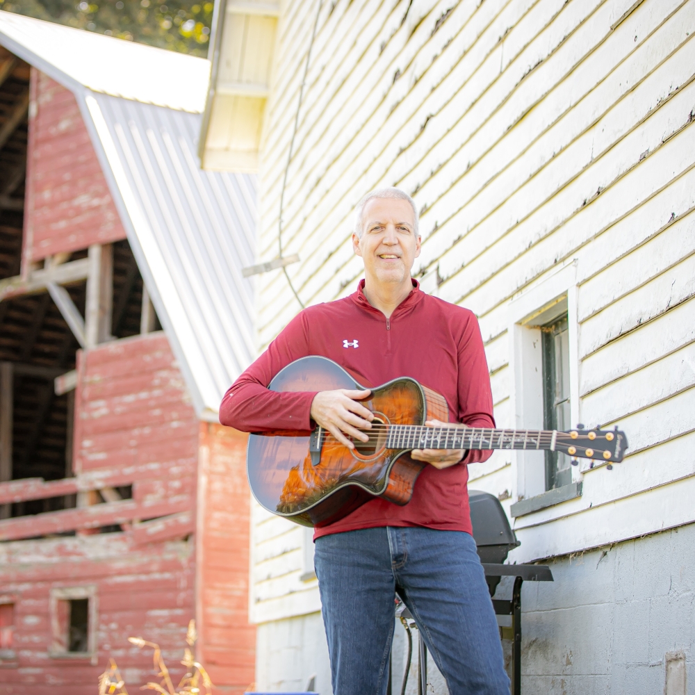 Mike Lucey Standing at White and Red Barns with a Breedlove Acoustic