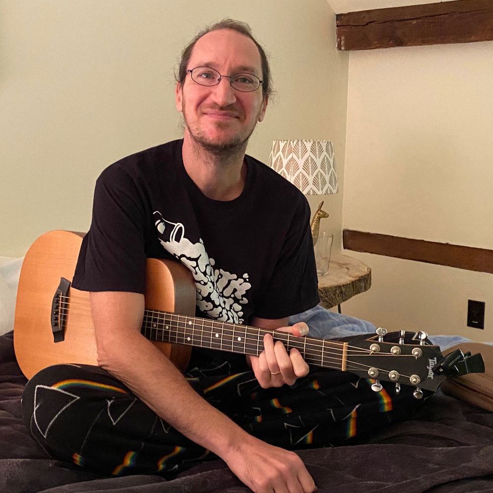 man with glasses and beard looking up smiling while holding guitar in bed brattleboro vermont