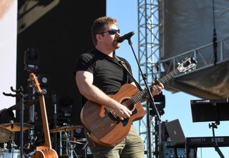 Derek Daisey playing acoustic guitar at an outdoor show