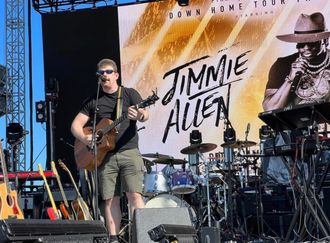 Derek Daisey singing and playing acoustic guitar on stage