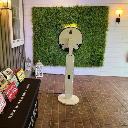 Crossroads Entertainment digital photo booth setup with a greenery backdrop and a table of wedding photo props.
