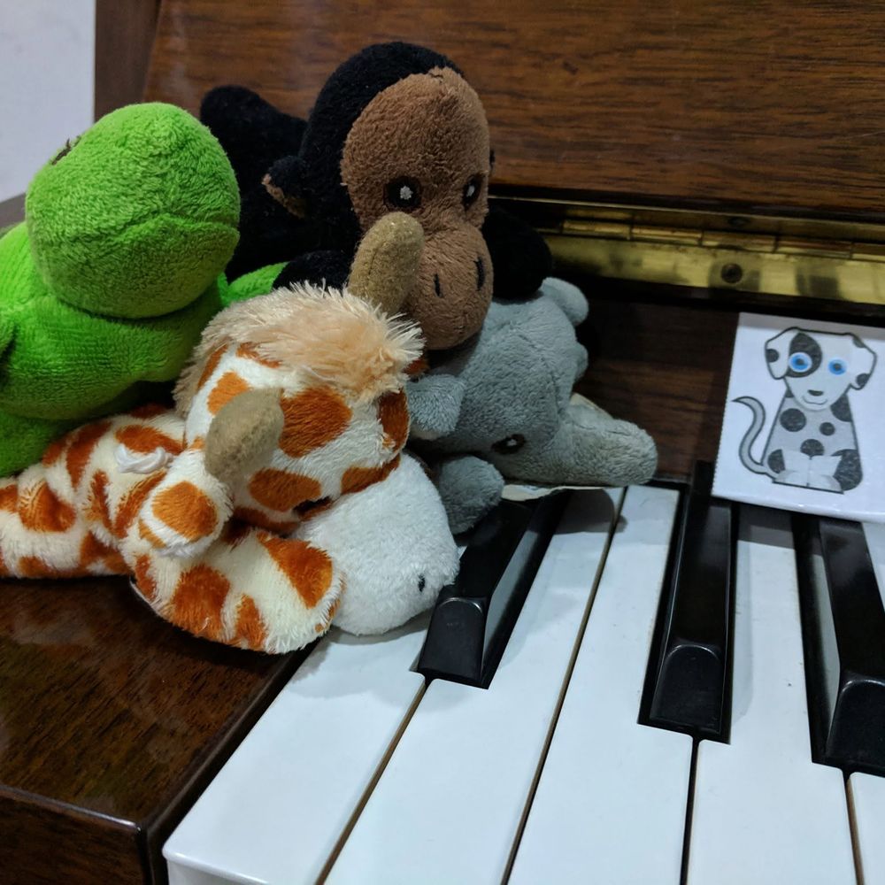 Animal toys and a dog illustration arranged beside an upright piano for a children’s music activity.