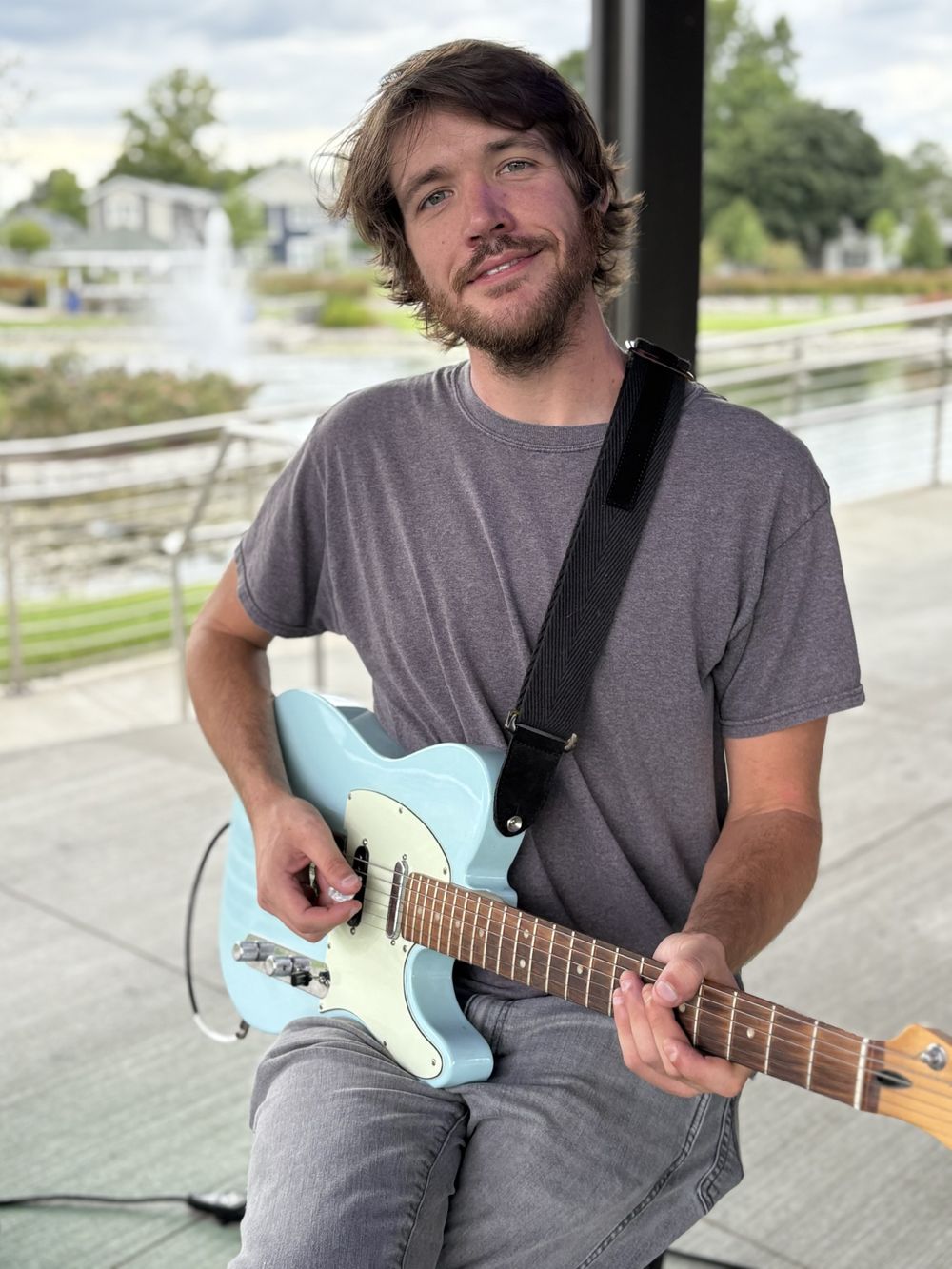 Sam Bennett sits with an electric guitar in front of a pond